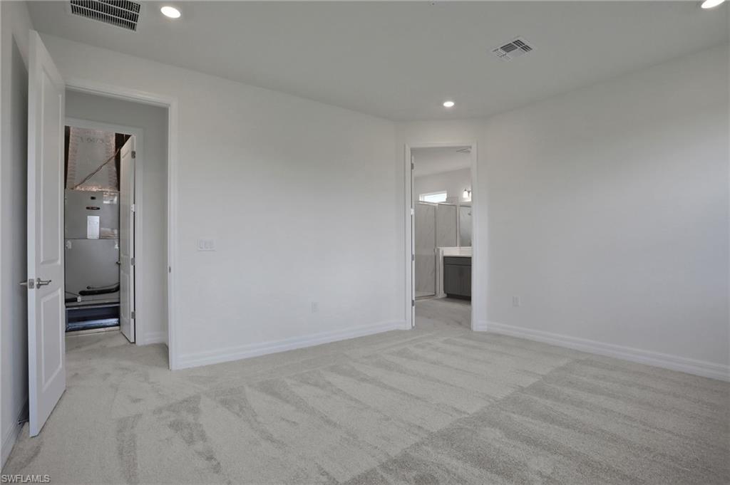 Unfurnished bedroom with light colored carpet, recessed lighting, connected bathroom, and heating unit