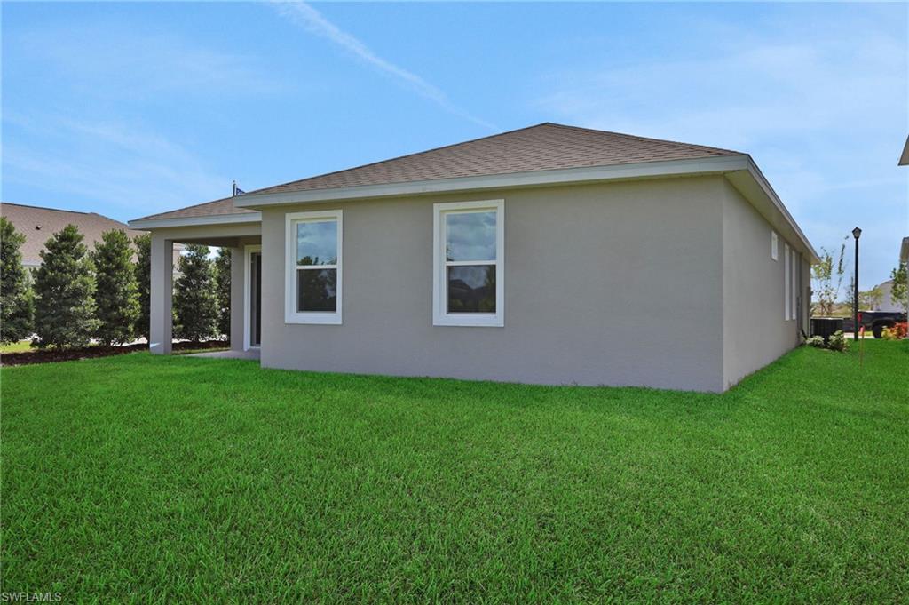 Rear view of house featuring a lawn, a shingled roof, a patio, and stucco siding