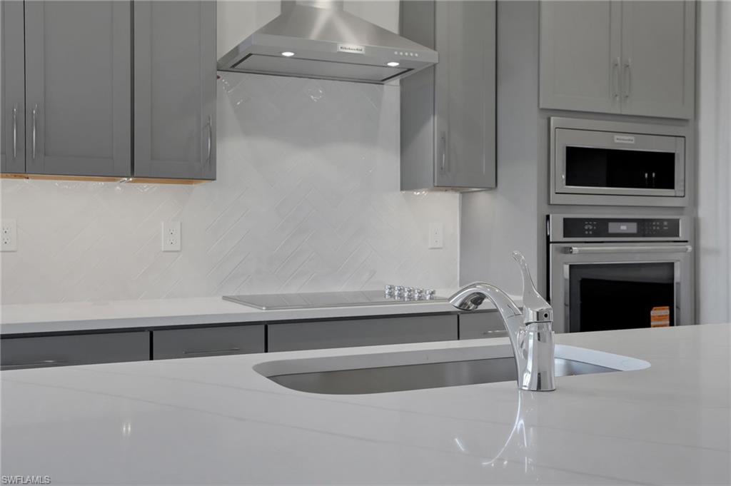 Kitchen with gray cabinets, light stone counters, stainless steel appliances, and backsplash