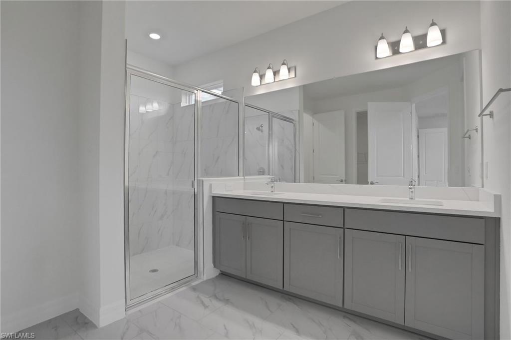 Full bathroom featuring double vanity, light marble finish floors, a marble finish shower, and recessed lighting