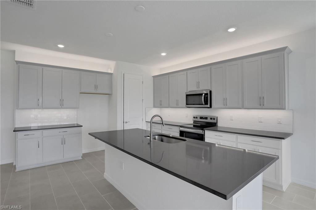Kitchen with decorative backsplash, stainless steel appliances, a center island with sink, recessed lighting, and dark stone countertops