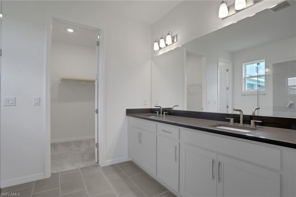 Bathroom with a walk in closet, double vanity, light tile patterned floors, and a shower