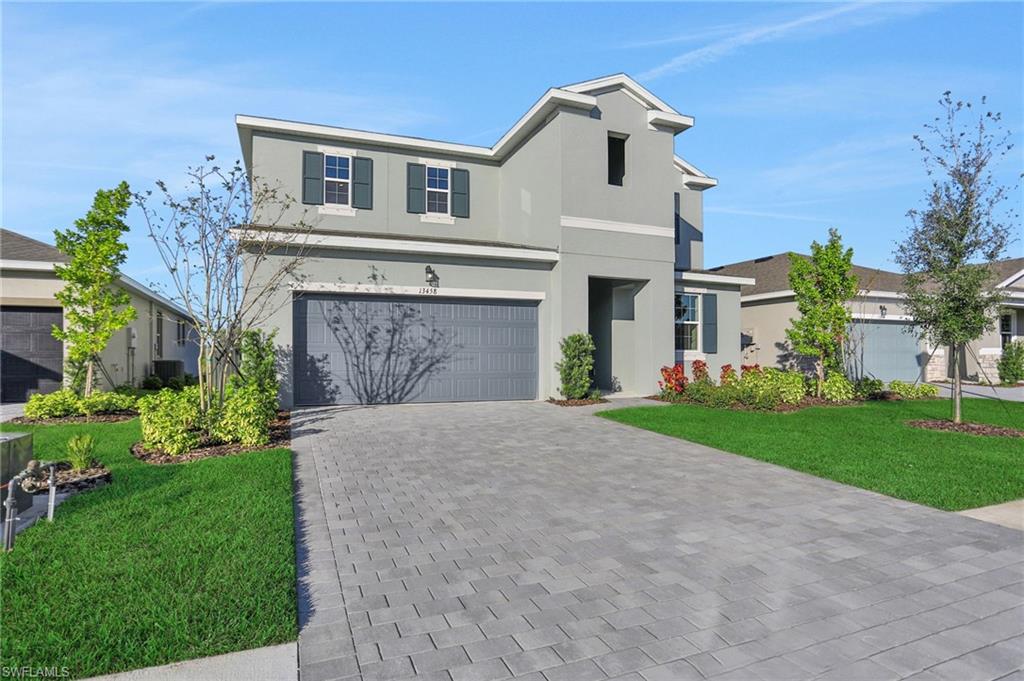 View of front of house with a front lawn, an attached garage, stucco siding, and decorative driveway