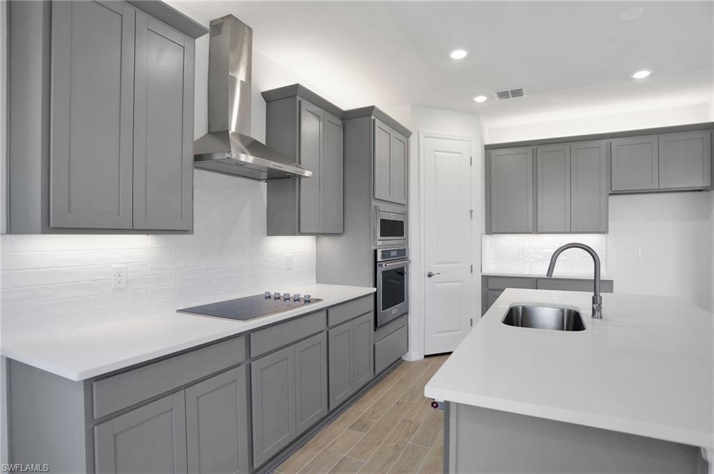 Kitchen with gray cabinetry, light stone counters, stainless steel appliances, wood tiled floors, and recessed lighting
