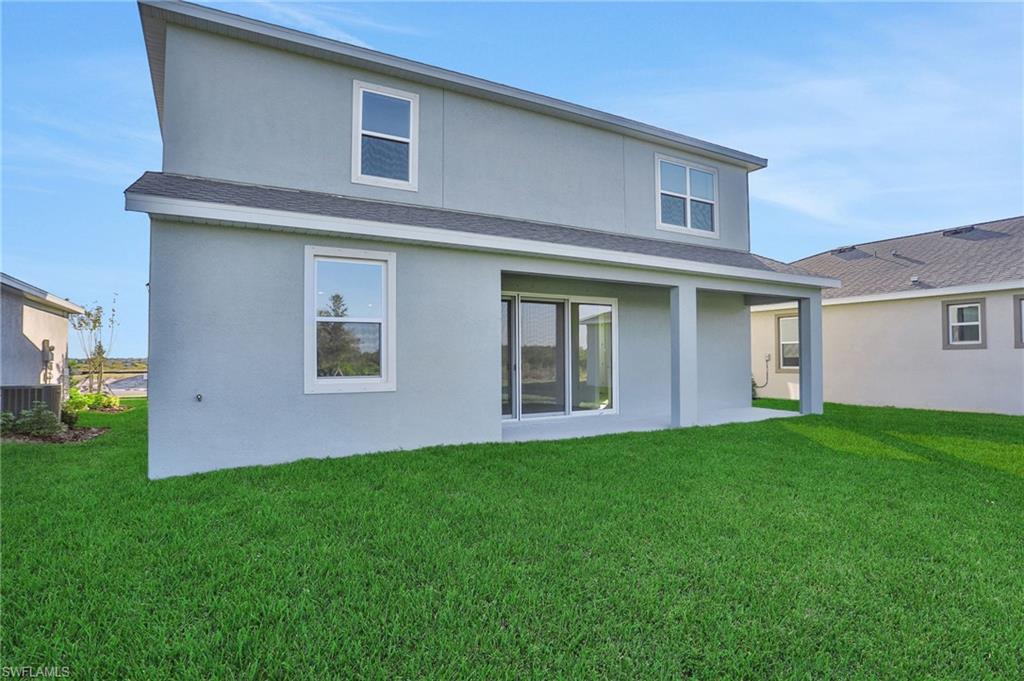 Rear view of house with a lawn, stucco siding, and a patio