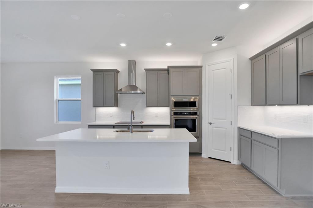 Kitchen featuring wood finish floors, gray cabinets, light stone counters, stainless steel appliances, and recessed lighting