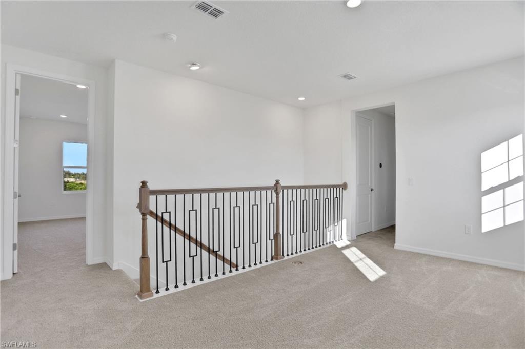 Hallway with an upstairs landing, light colored carpet, and recessed lighting