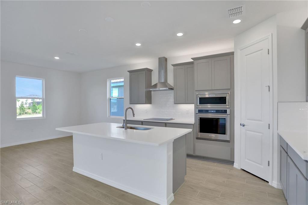 Kitchen with gray cabinets, stainless steel appliances, recessed lighting, wood finish floors, and a kitchen island with sink