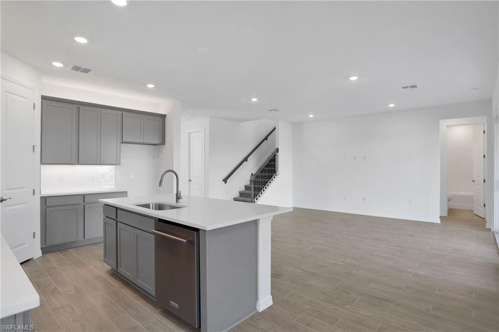 Kitchen with wood finish floors, gray cabinetry, recessed lighting, stainless steel dishwasher, and a kitchen island with sink