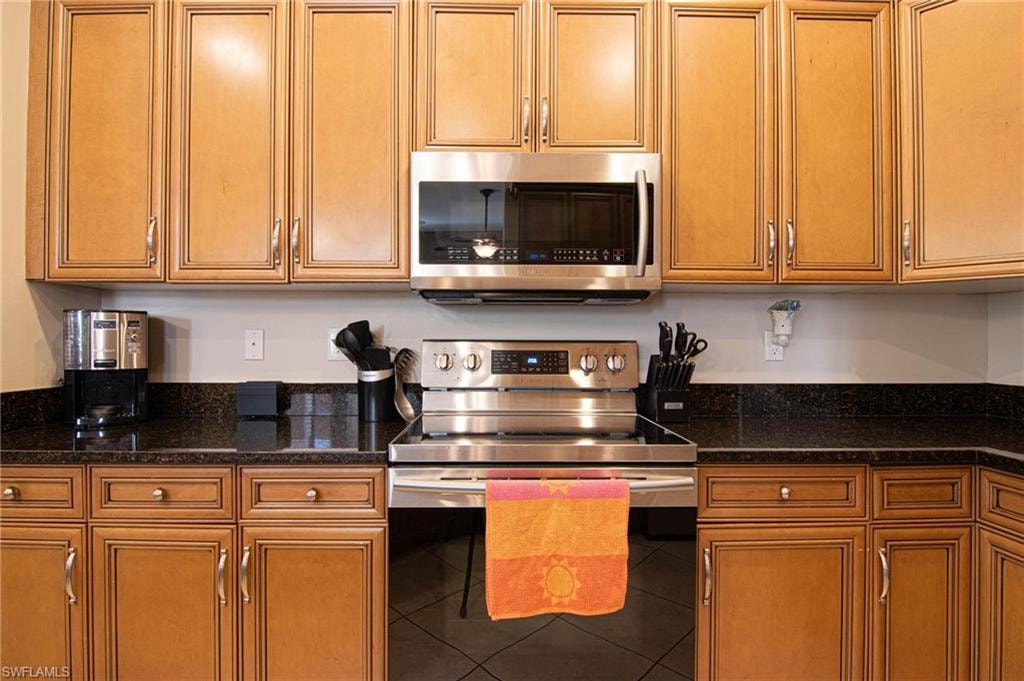 Kitchen featuring stainless steel appliances, wood finish cabinets, and dark stone counters