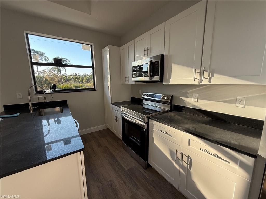 Kitchen with stainless steel appliances, dark stone counters, and white cabinetry