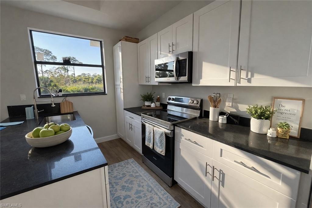 Kitchen with stainless steel appliances, white cabinetry, dark stone countertops, and dark wood-style floors
