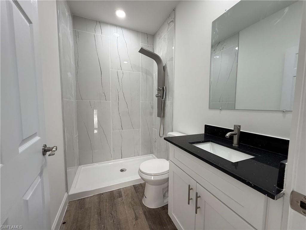 Full bath with a tile shower, vanity, dark wood-type flooring, and recessed lighting
