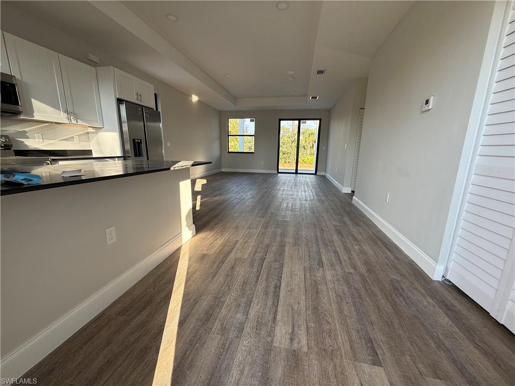 Kitchen with white cabinetry, stainless steel appliances, a kitchen bar, dark wood-style floors, and open floor plan