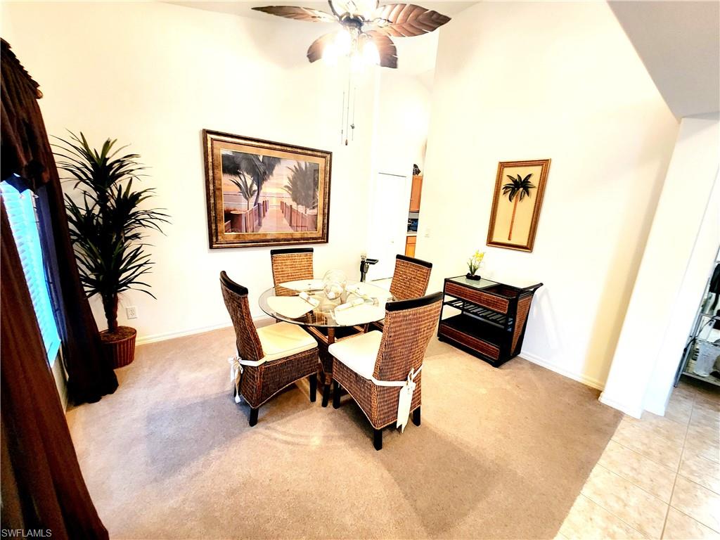 Dining space featuring a high ceiling, light colored carpet, ceiling fan, a barn door, and light tile patterned floors