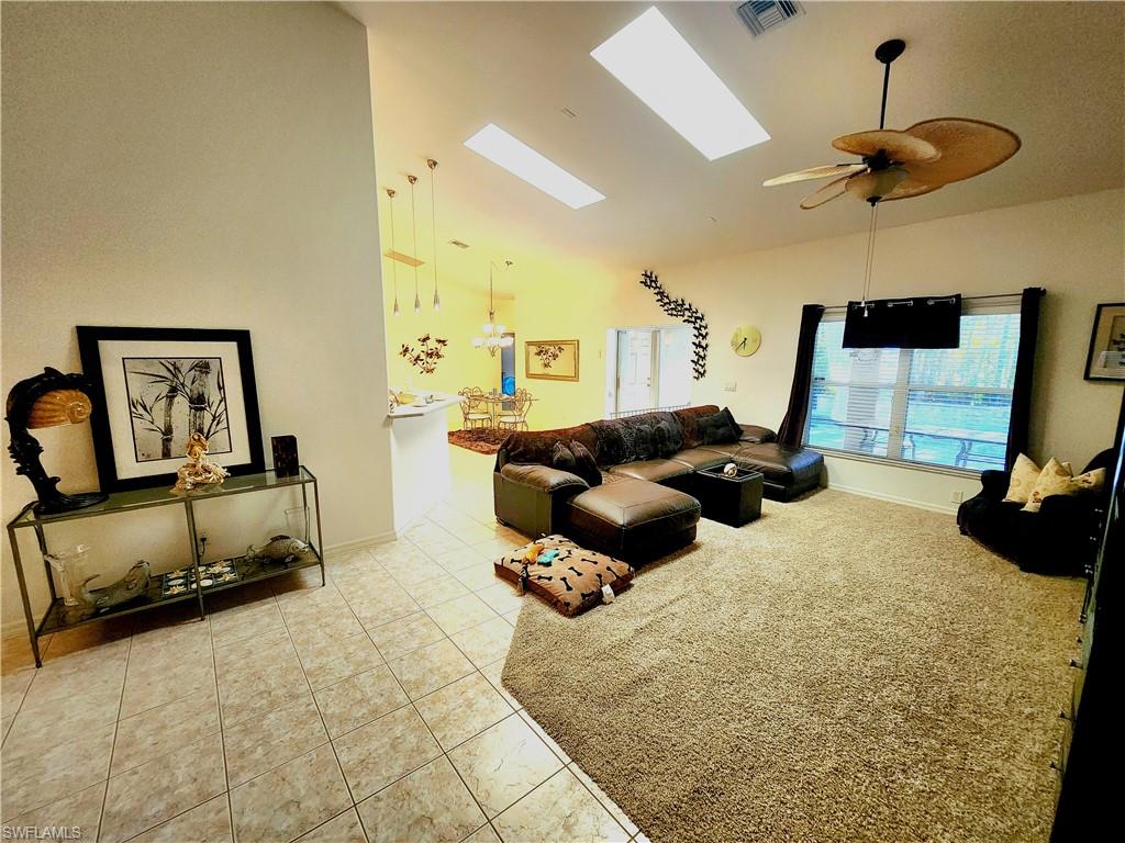 Living room with vaulted ceiling, light tile patterned floors, a skylight, and ceiling fan