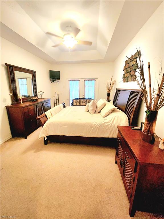 Bedroom featuring light colored carpet, a tray ceiling, and ceiling fan