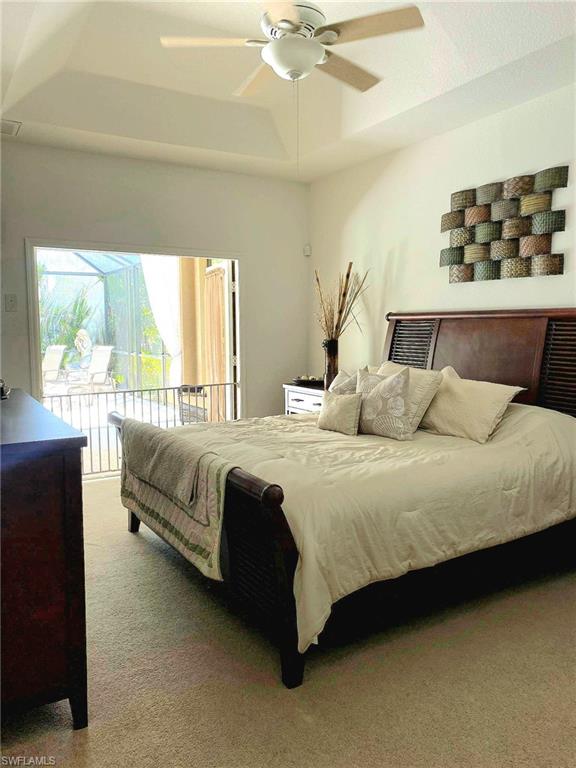 Carpeted bedroom with a raised ceiling, ceiling fan, and access to outside