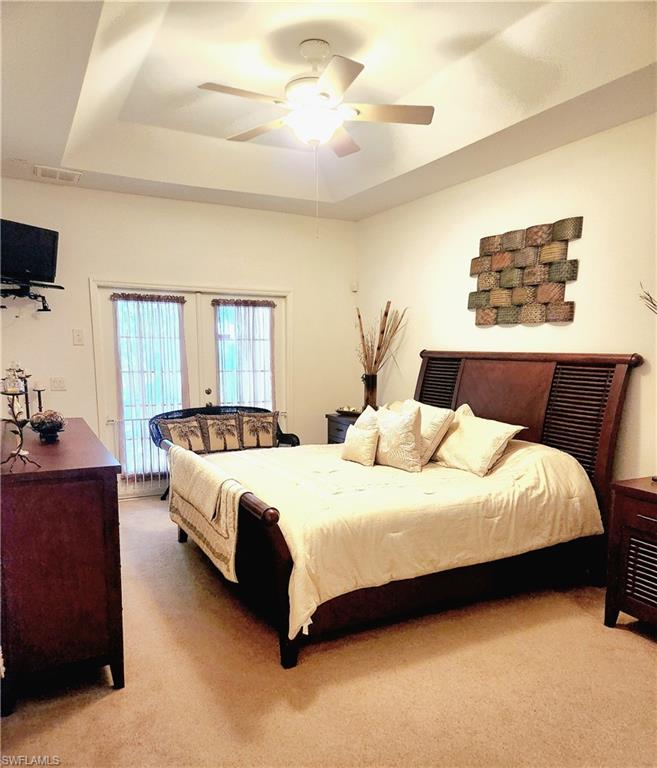 Bedroom with light colored carpet, access to outside, french doors, a raised ceiling, and a ceiling fan