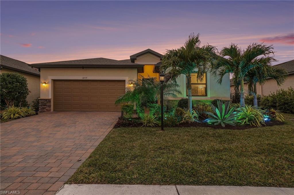 View of front facade featuring stucco siding, a lawn, driveway, stone siding, and a garage