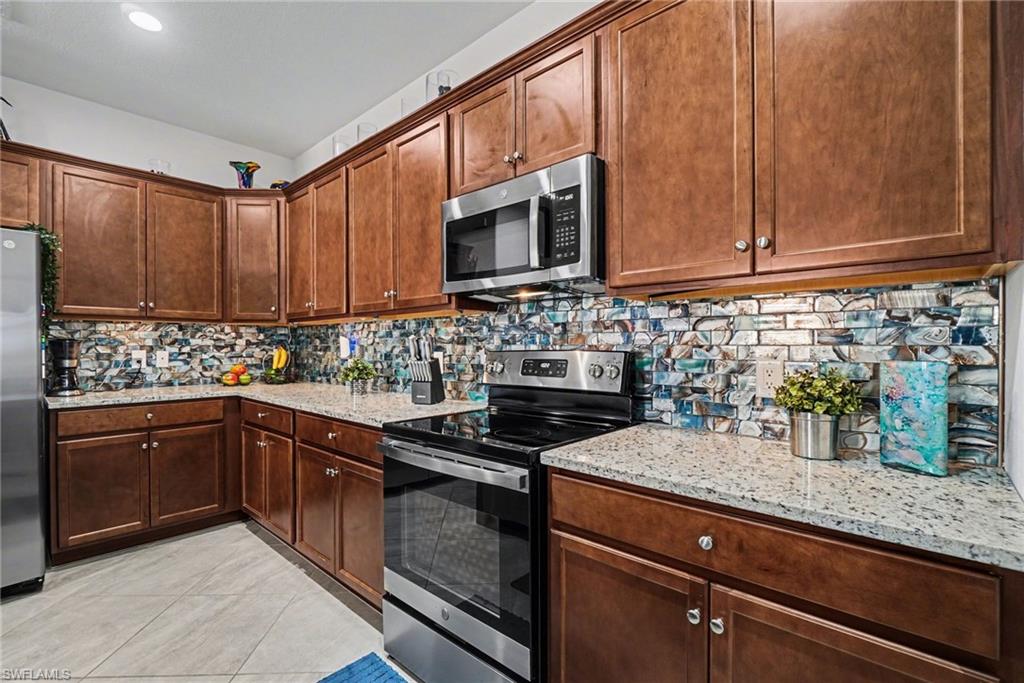 Kitchen featuring stainless steel appliances, light stone countertops, backsplash, and light tile patterned floors