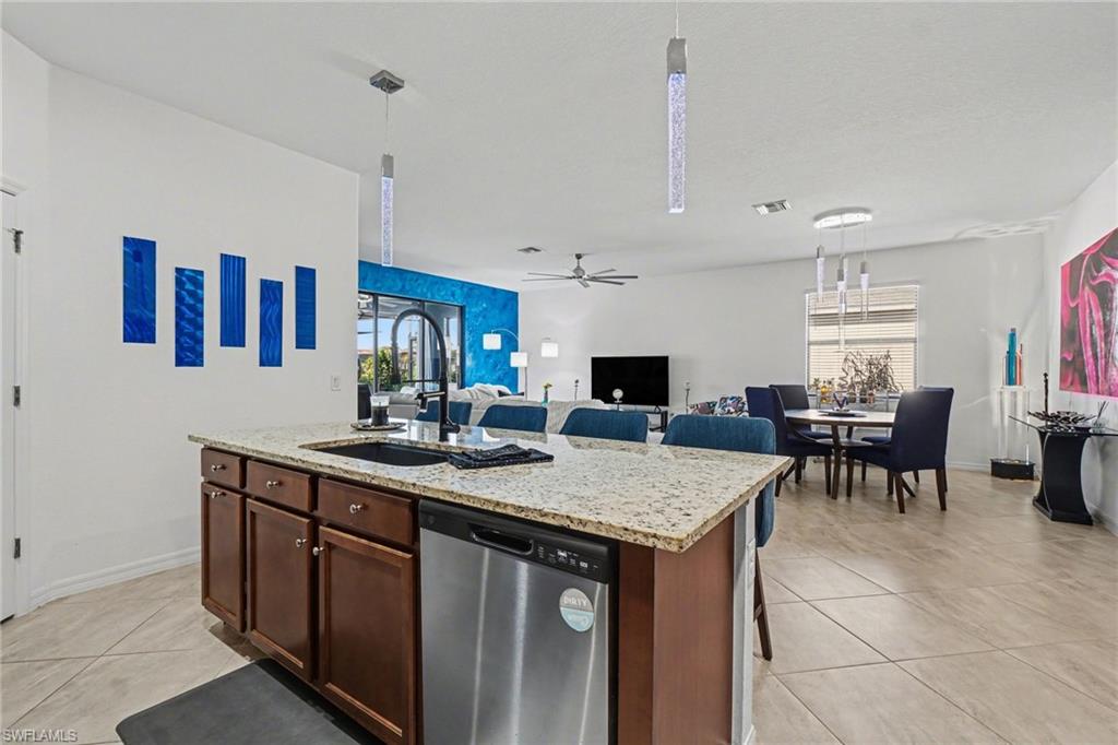 Kitchen featuring stainless steel dishwasher, light stone countertops, pendant lighting, and a center island with sink