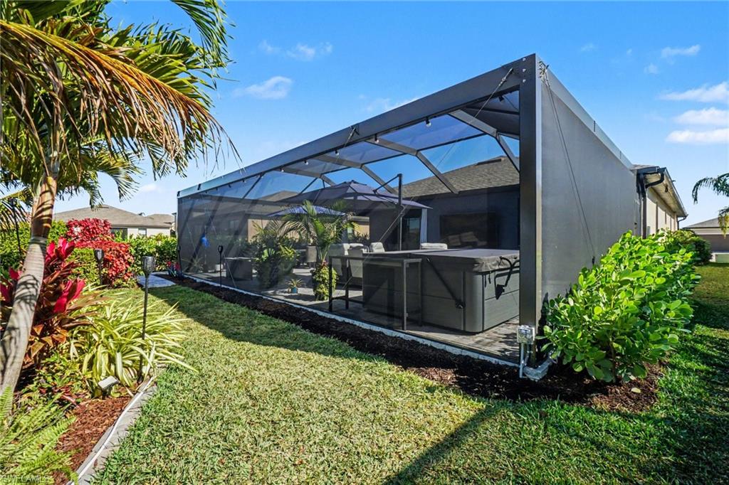 Rear view of property featuring a yard, glass enclosure, a sunroom, and a hot tub