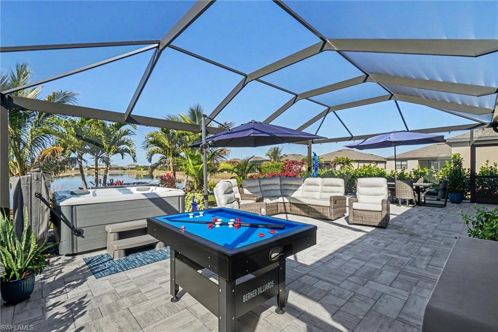 View of patio / terrace featuring glass enclosure, a hot tub, a sunroom, an outdoor lounge area, and a water view