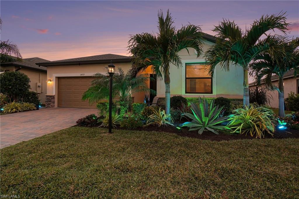 View of front of house with a lawn, stucco siding, decorative driveway, and stone siding