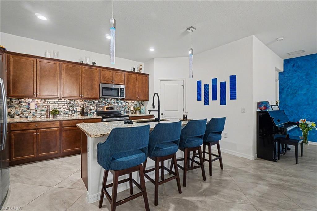 Kitchen featuring a kitchen breakfast bar, an island with sink, light stone countertops, stainless steel appliances, and decorative light fixtures