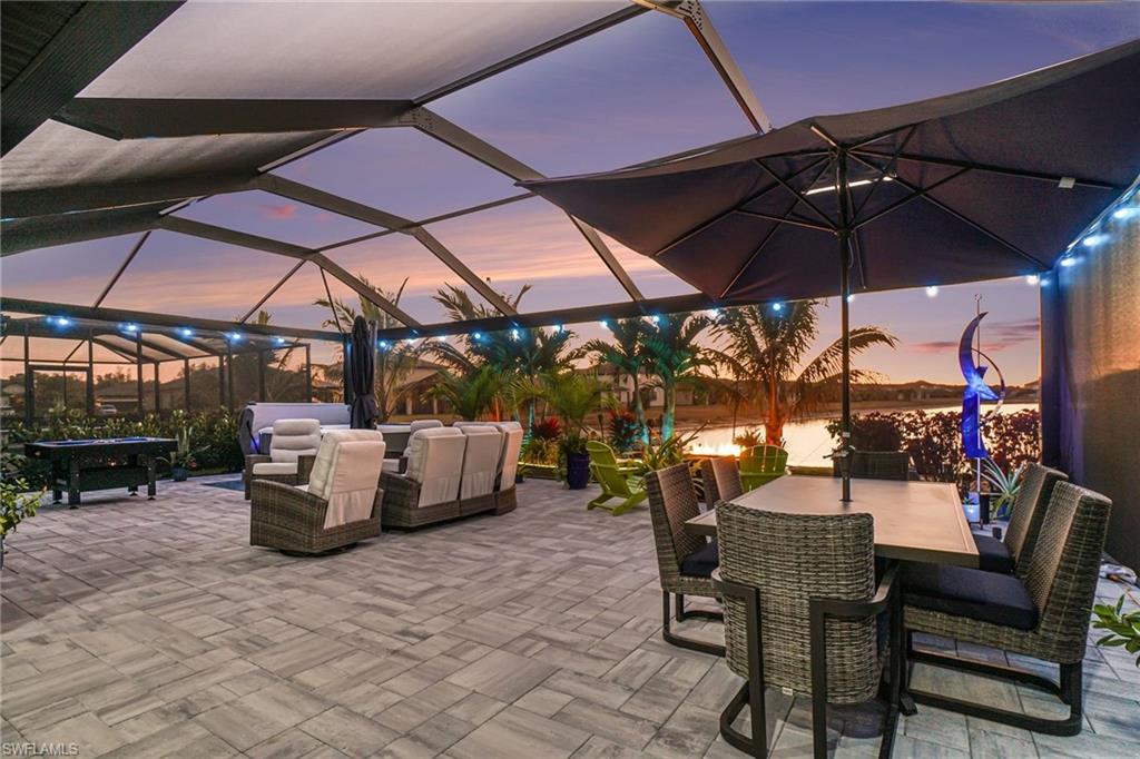 Patio terrace at dusk featuring an outdoor living / dining area, a sunroom, a patio area, glass enclosure, and a water view