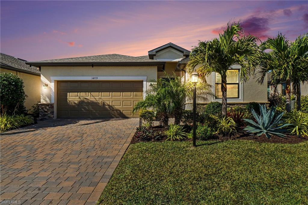 View of front of home featuring stucco siding, decorative driveway, a front lawn, and a garage