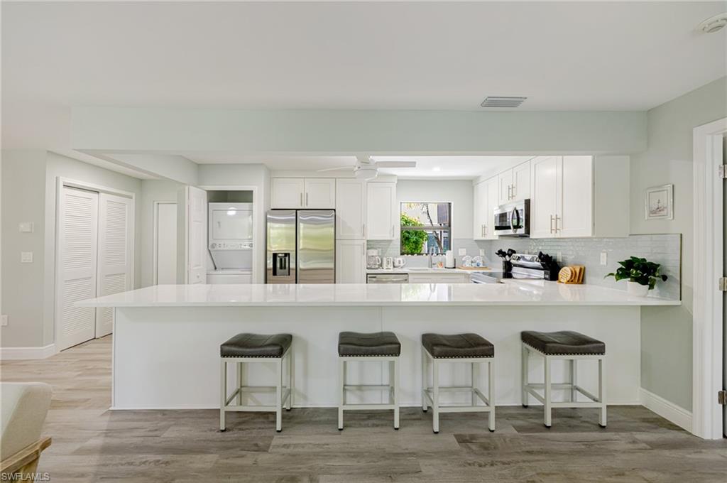 Kitchen featuring a peninsula, stainless steel appliances, white cabinetry, a breakfast bar area, and light wood-style floors