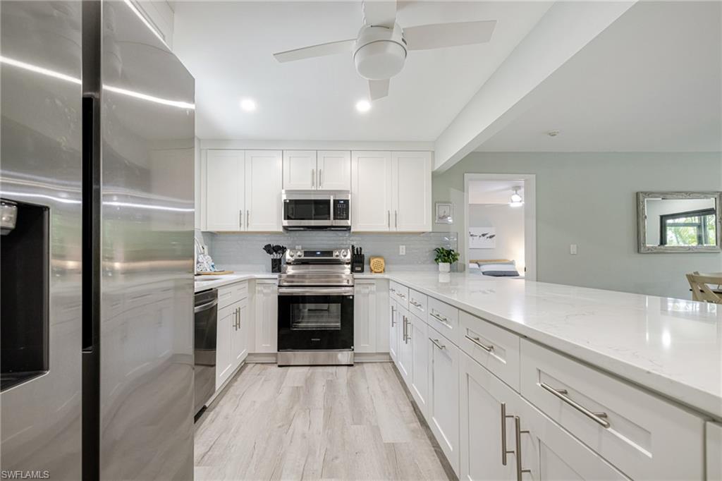 Kitchen featuring stainless steel appliances, white cabinetry, light stone counters, ceiling fan, and recessed lighting