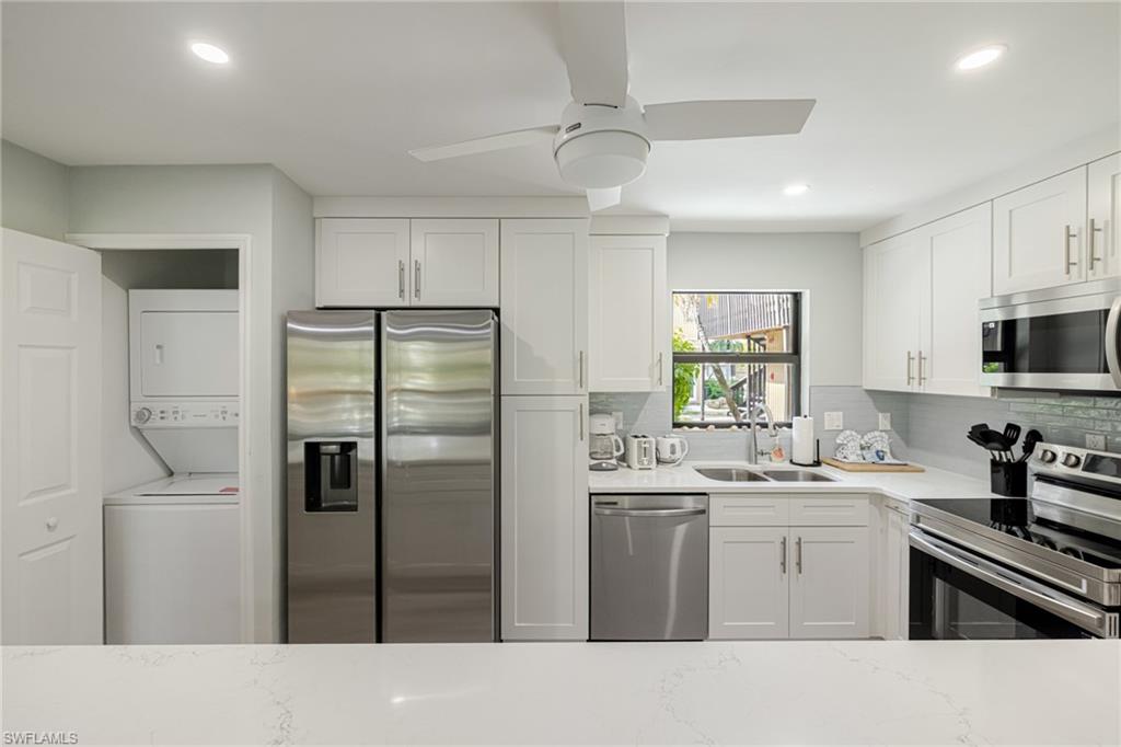Kitchen with stainless steel appliances, white cabinets, light stone countertops, stacked washer / drying machine, and recessed lighting
