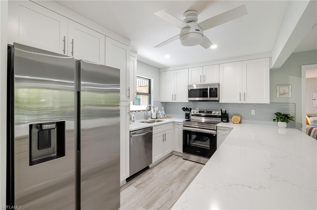 Kitchen with stainless steel appliances, white cabinetry, light stone counters, a ceiling fan, and light wood finished floors