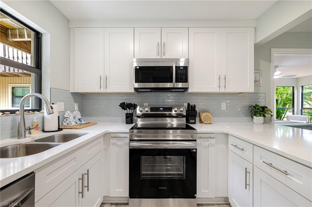 Kitchen featuring stainless steel appliances, white cabinets, light stone countertops, and backsplash