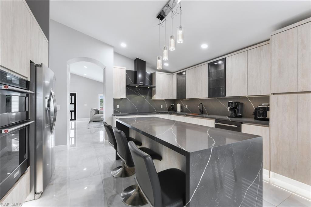 Kitchen featuring a breakfast bar area, modern cabinets, dark stone counters, decorative light fixtures, and black appliances