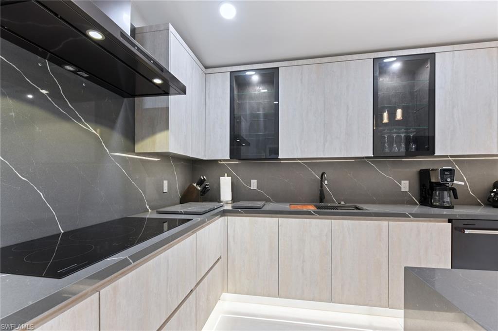 Kitchen with light wood finish cabinets, modern cabinets, extractor fan, dark stone counters, and backsplash