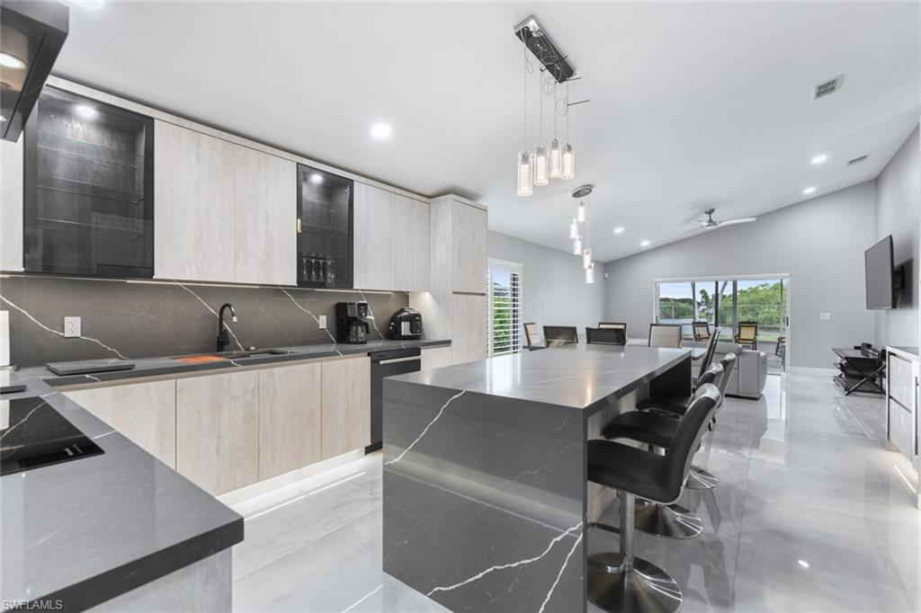 Kitchen with pendant lighting, a breakfast bar, modern cabinets, range hood, and vaulted ceiling