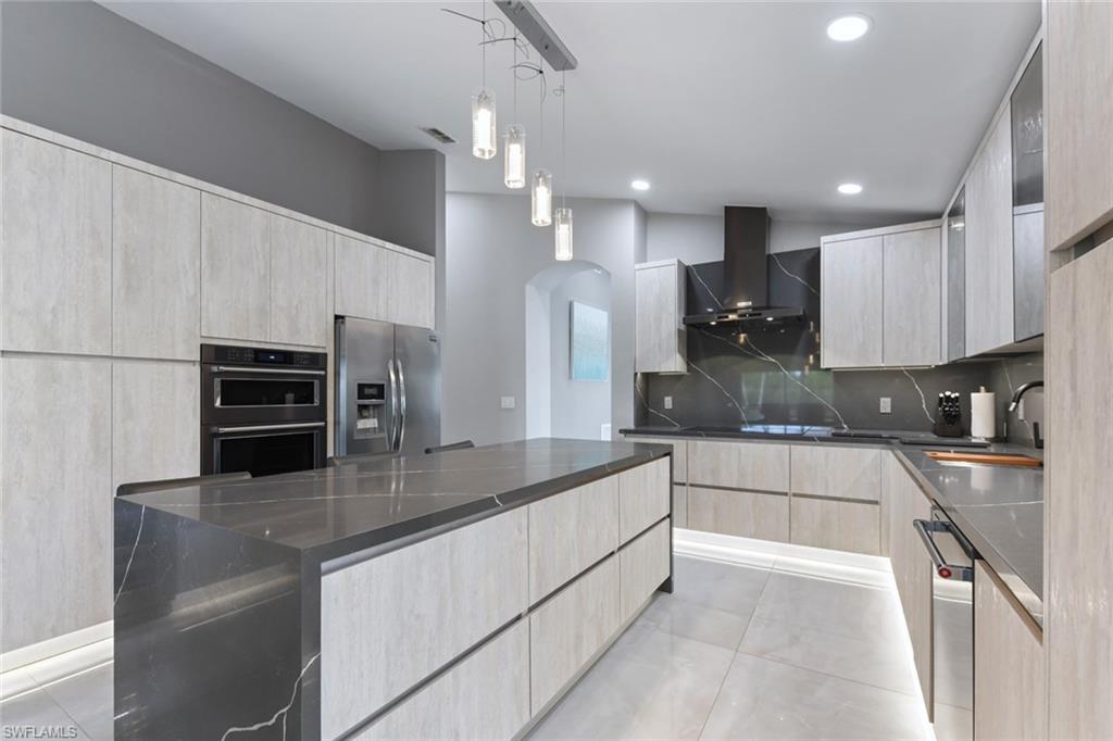 Kitchen featuring light wood finish cabinets, stainless steel appliances, dark stone counters, and decorative light fixtures