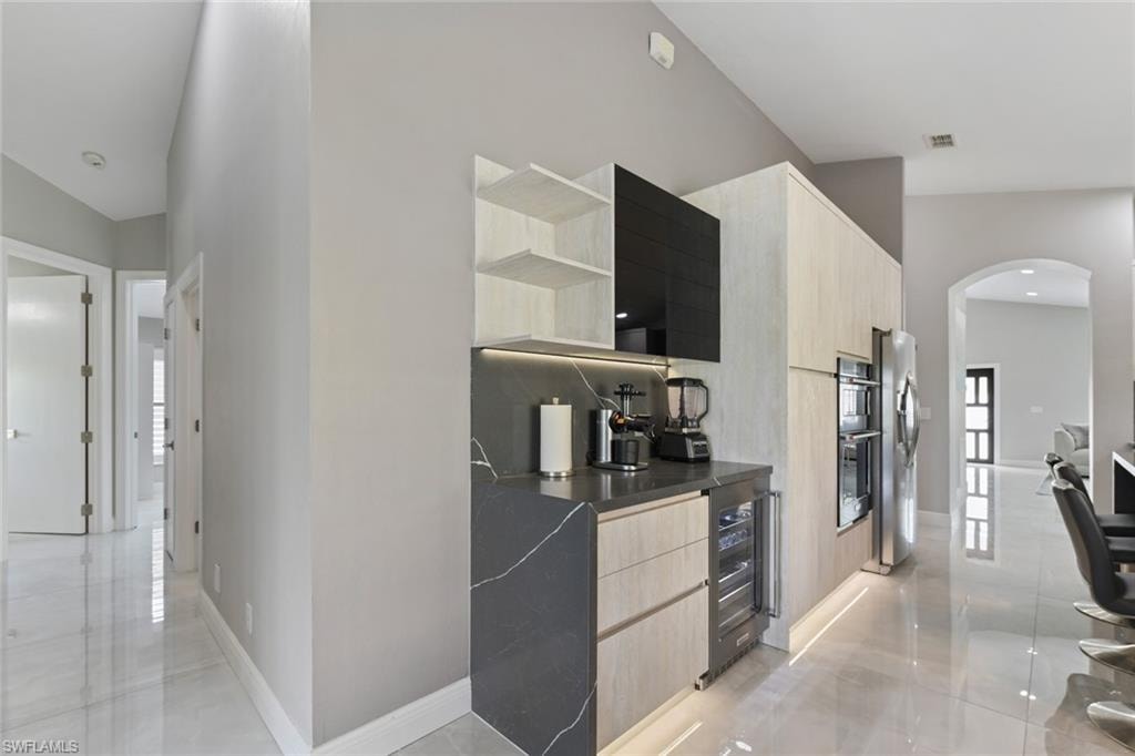 Kitchen featuring open shelves, arched walkways, light wood finish cabinets, modern cabinets, and wine cooler