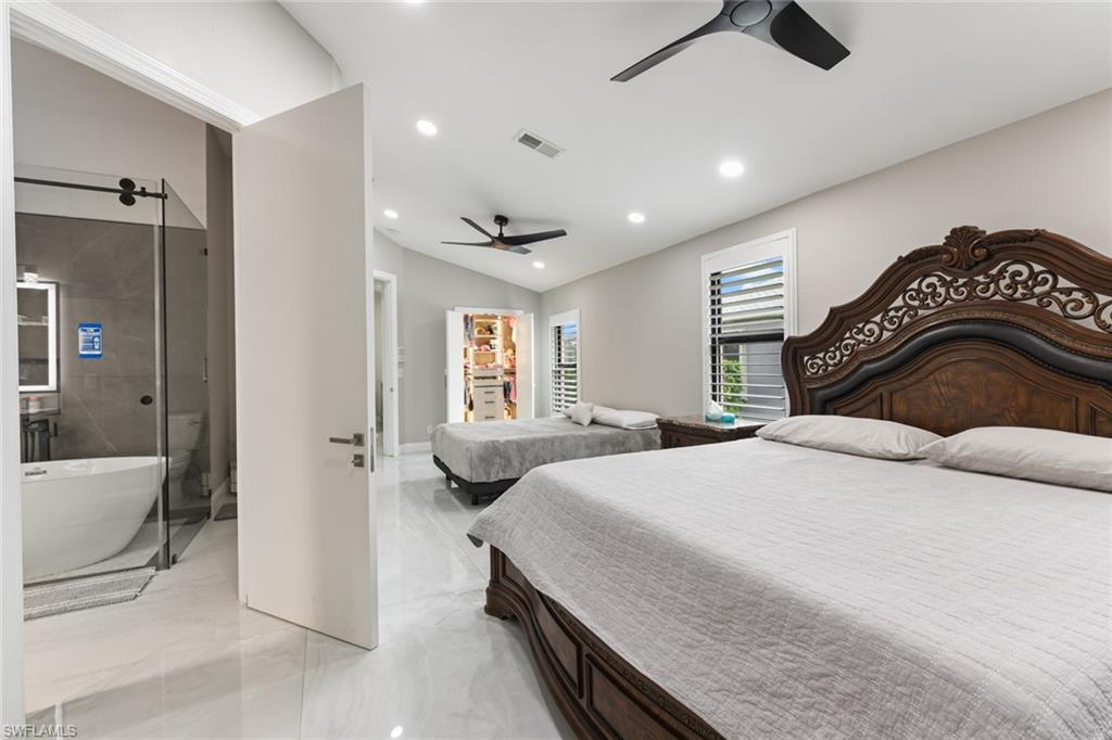 Bedroom featuring ensuite bathroom, lofted ceiling, a ceiling fan, recessed lighting, and light marble finish floors