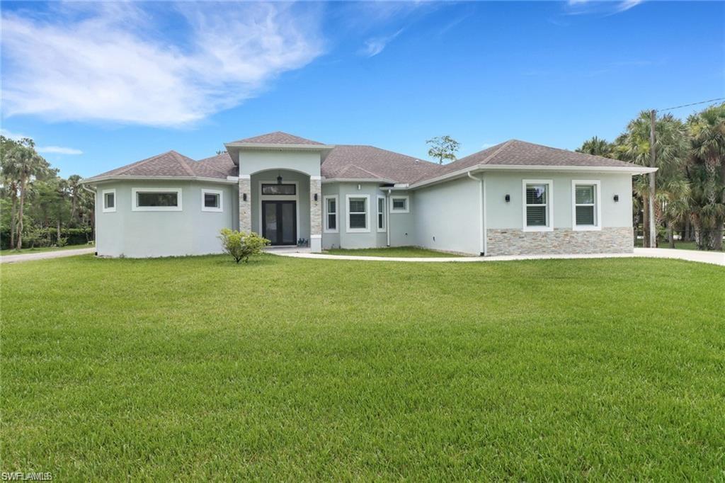 View of front of home with stucco siding, a front lawn, and stone siding