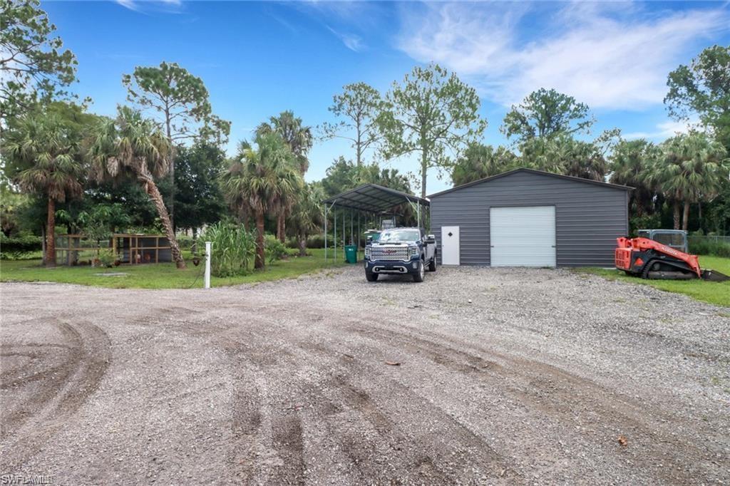 Detached garage with driveway, a detached carport, and view of scattered trees