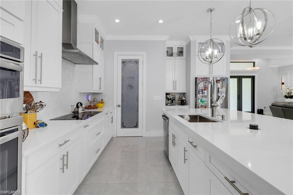 Kitchen with white cabinetry, glass insert cabinets, stainless steel appliances, crown molding, and light stone counters