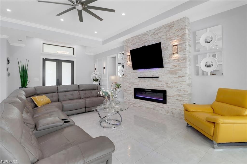 Living room featuring a stone fireplace, ceiling fan, french doors, ornamental molding, and recessed lighting