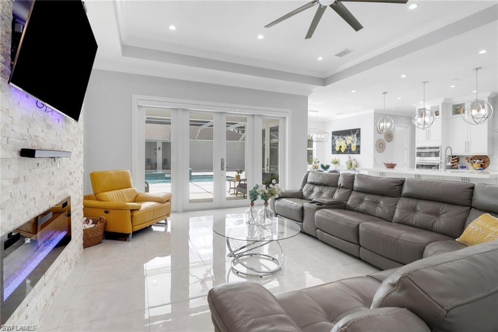 Living area featuring a stone fireplace, a tray ceiling, a ceiling fan, and suspended lighting