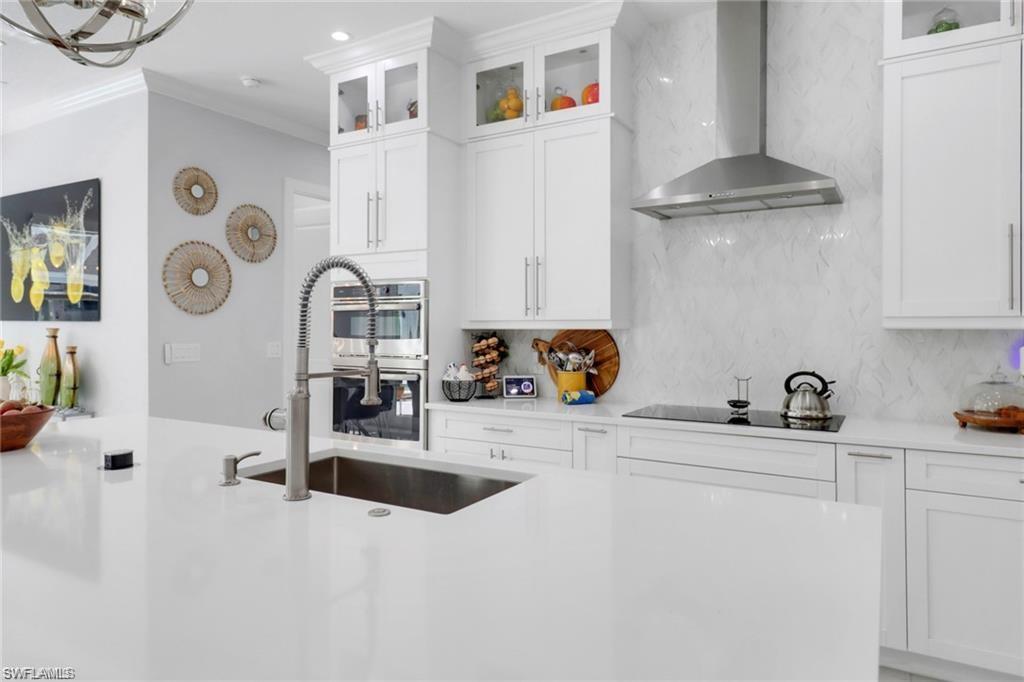 Kitchen featuring white cabinets, glass insert cabinets, crown molding, backsplash, and light stone counters