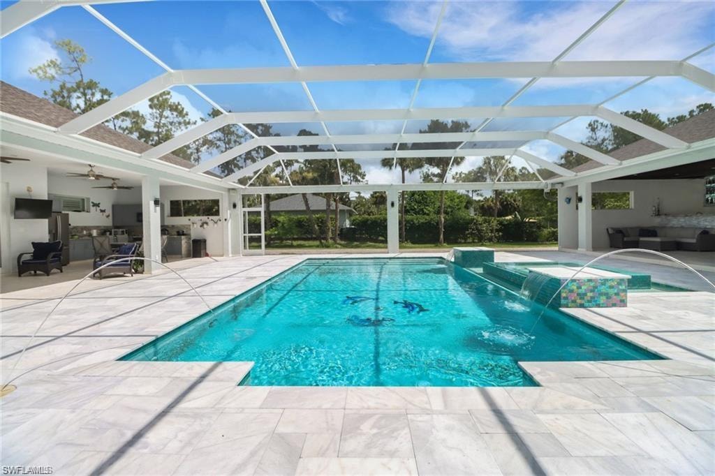 Swimming pool featuring an outdoor kitchen with living area, a patio area, glass enclosure, and a sunroom